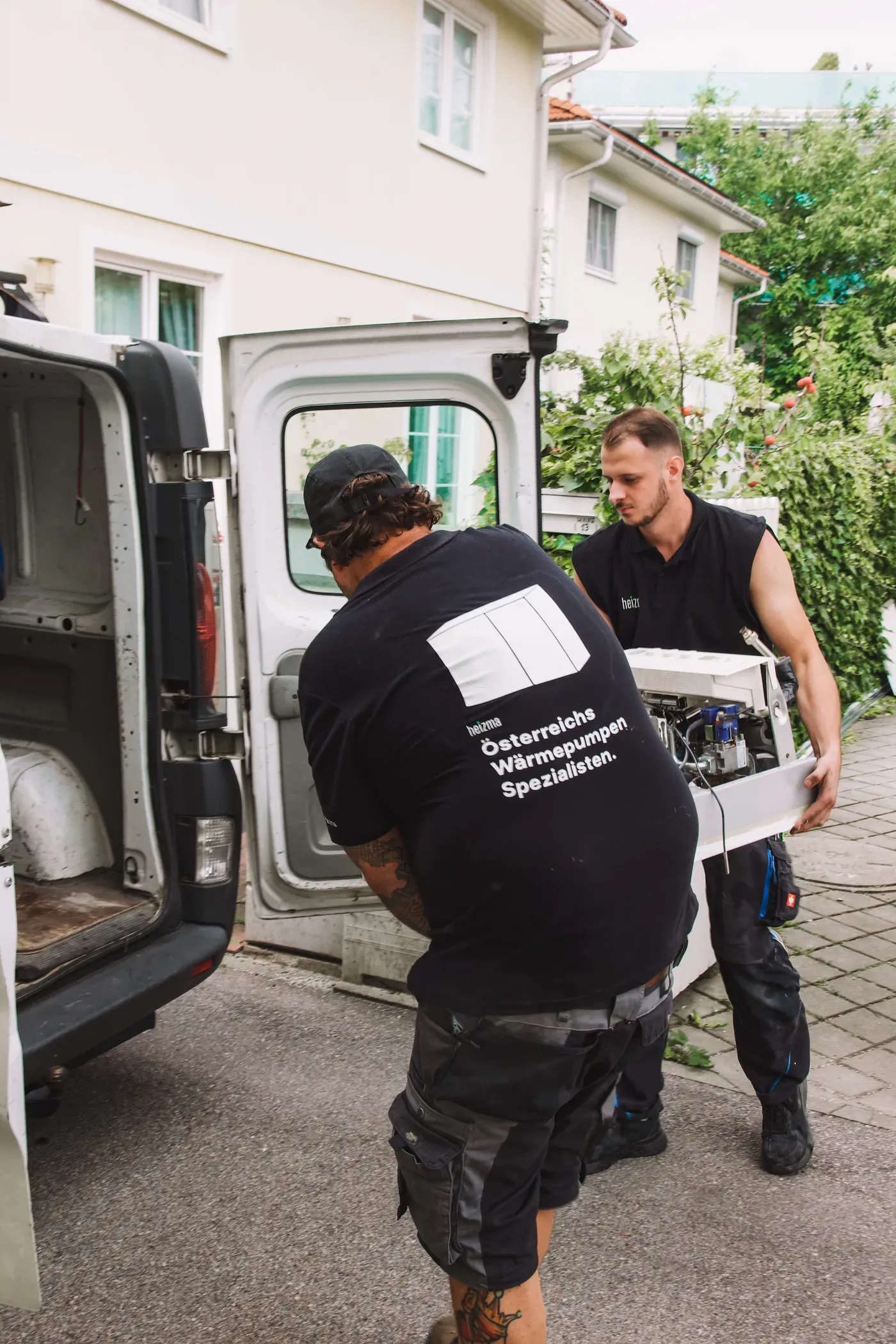 Zwei Heizma-Techniker laden ein Wärmepumpen-Bauteil aus dem Transporter
