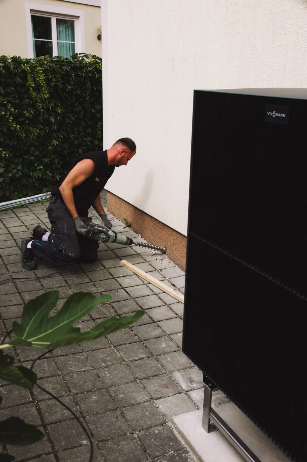 Heizma-Techniker bohrt die Außenwand neben einer Viessmann-Wärmepumpe