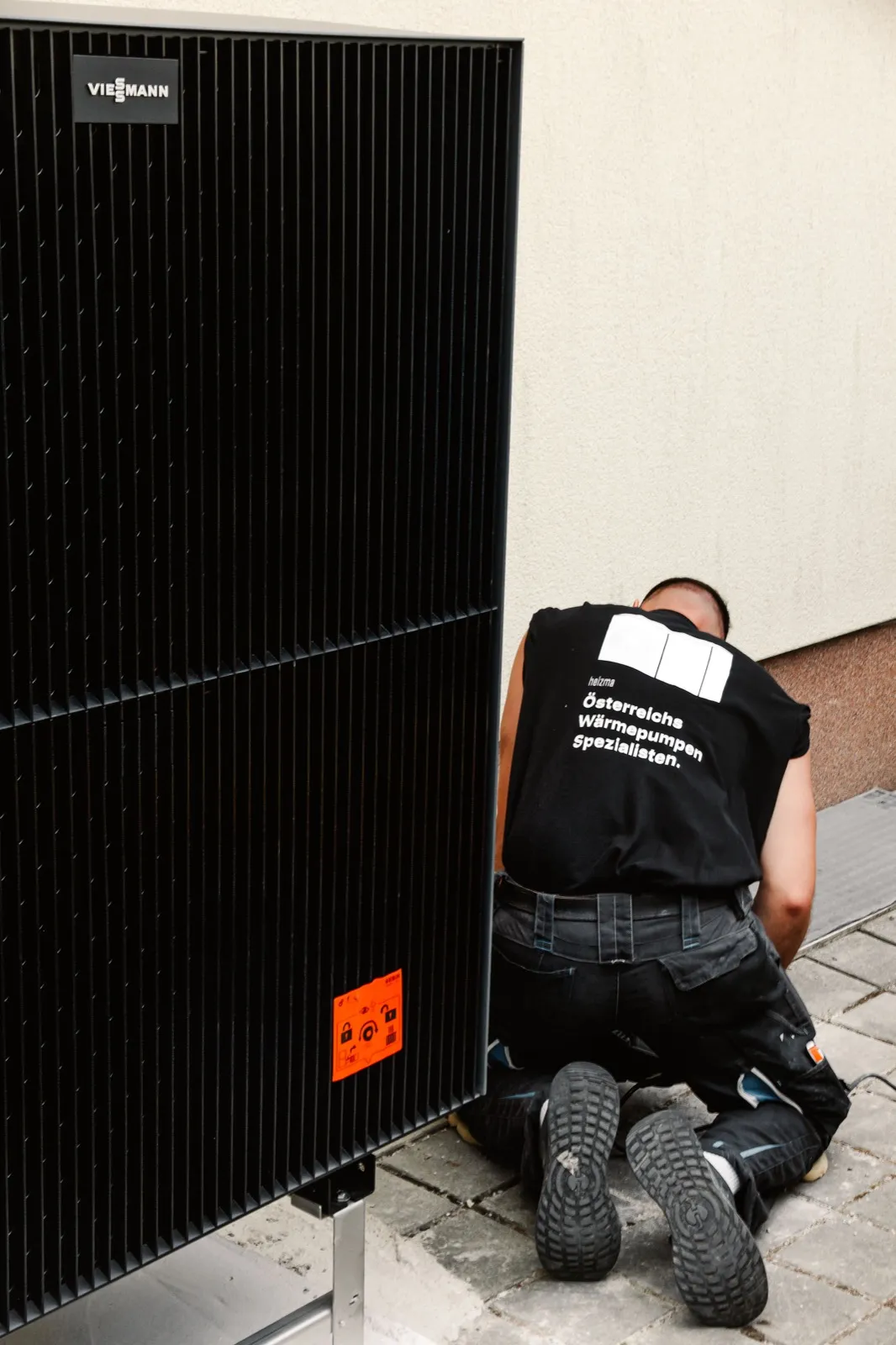 Heizma-Techniker montiert eine schwarze Viessmann-Wärmepumpe an der Hausfassade