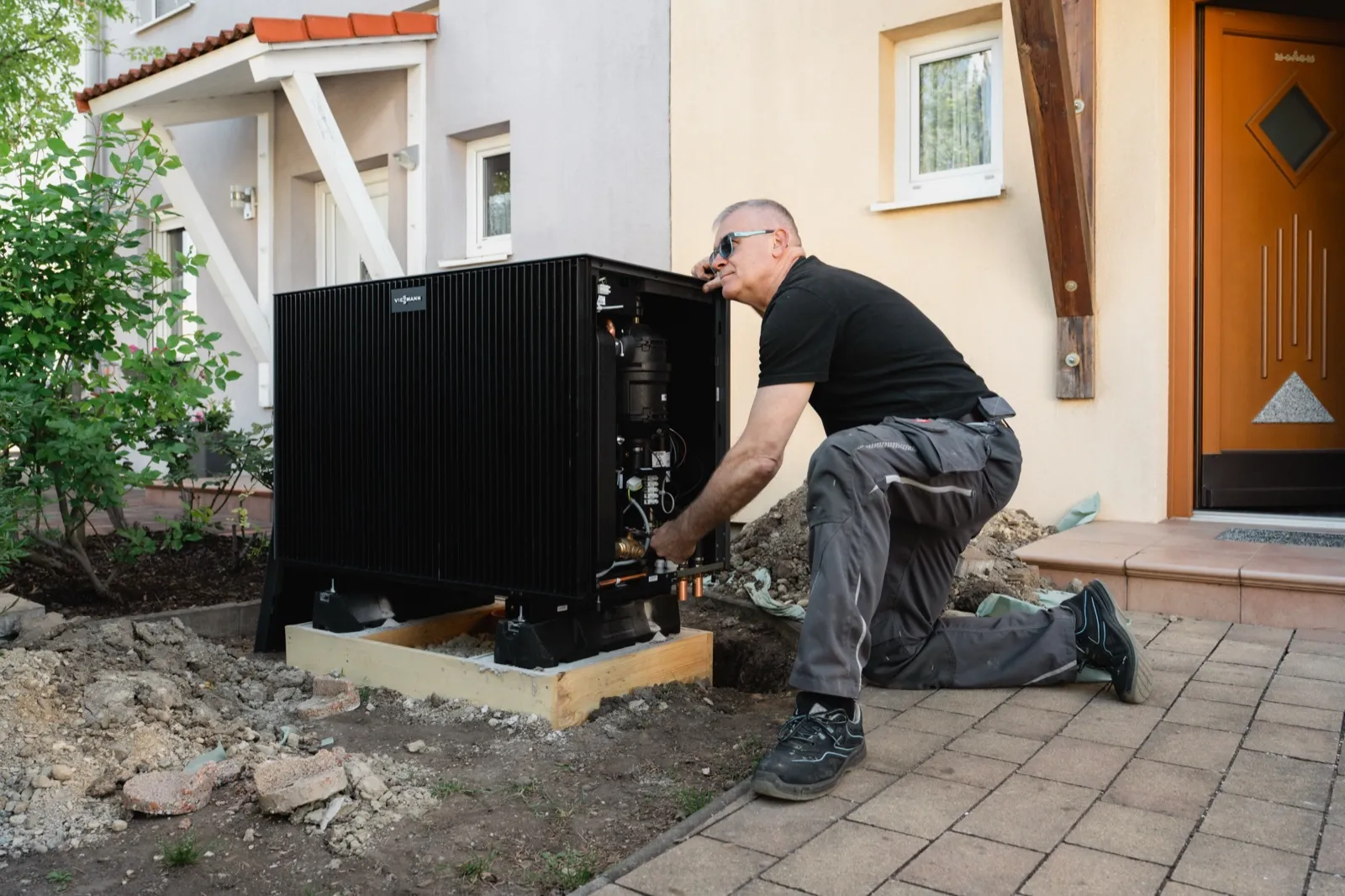 Heizma-Techniker kniet vor einer geöffneten Viessmann-Wärmepumpe und schließt sie an